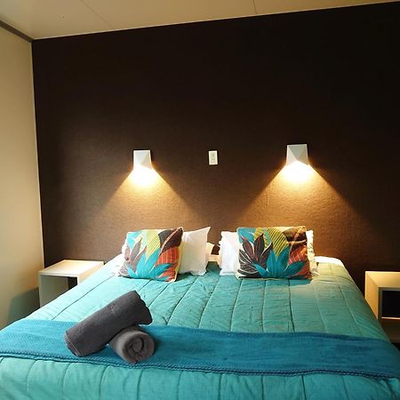 タウポ デブレッツ スパ リゾート エクステリア 写真 The image shows a bedroom with a modern and inviting layout. The focal point is a bed with a vibrant turquoise comforter, decorated with two colorful pillows featuring floral patterns. On either side of the bed, there are small nightstands with wall-