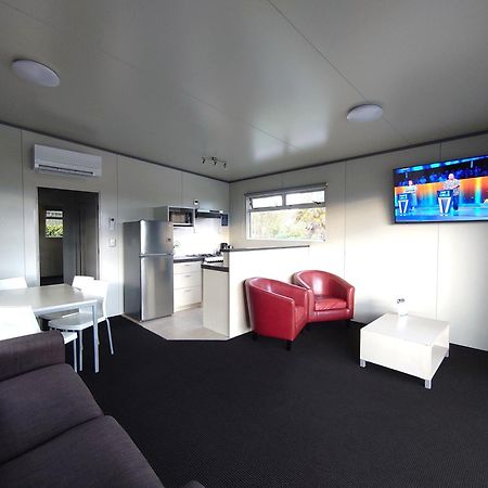 タウポ デブレッツ スパ リゾート エクステリア 写真 The photo displays a modern, compact living space. It features a small kitchen area with a refrigerator and cabinets on one side. A dining table with white chairs is set up in the center of the room. On the opposite side, there is a comfortable dark 