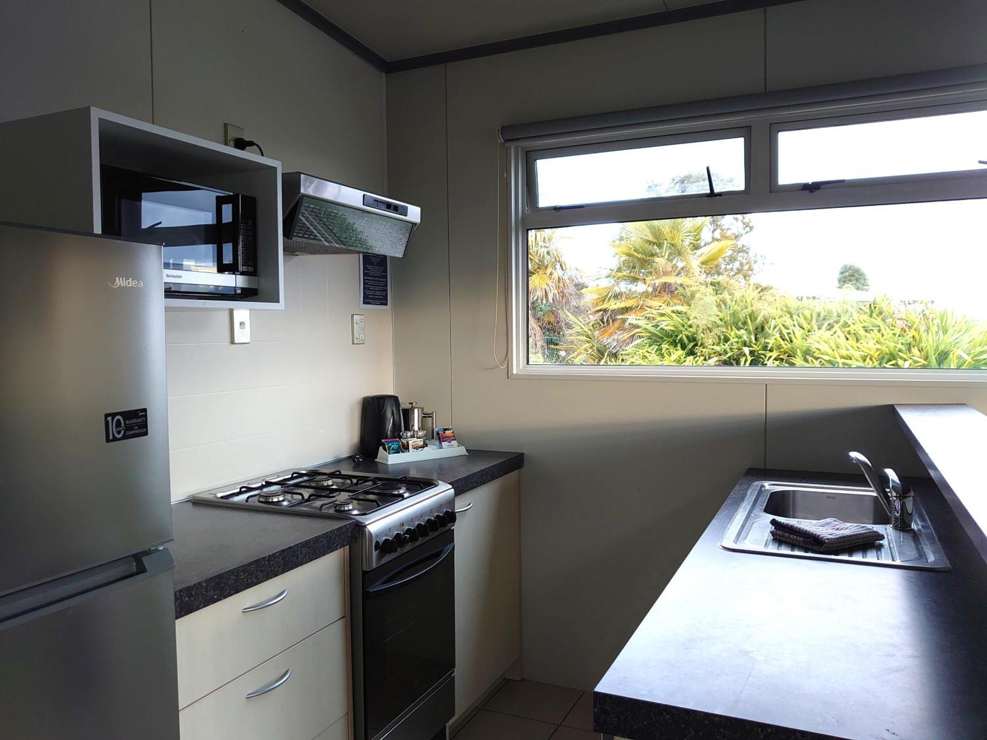 タウポ デブレッツ スパ リゾート エクステリア 写真 The photo shows a kitchen equipped with modern appliances. On the left side, there is a refrigerator and a microwave above it. The kitchen features a gas stove with a range hood above. To the right, there is a kitchen sink with a countertop. A window