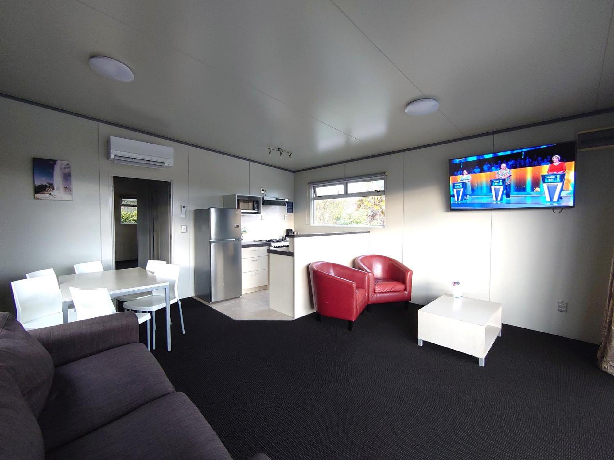 タウポ デブレッツ スパ リゾート エクステリア 写真 The photo displays a modern, compact living space. It features a small kitchen area with a refrigerator and cabinets on one side. A dining table with white chairs is set up in the center of the room. On the opposite side, there is a comfortable dark 